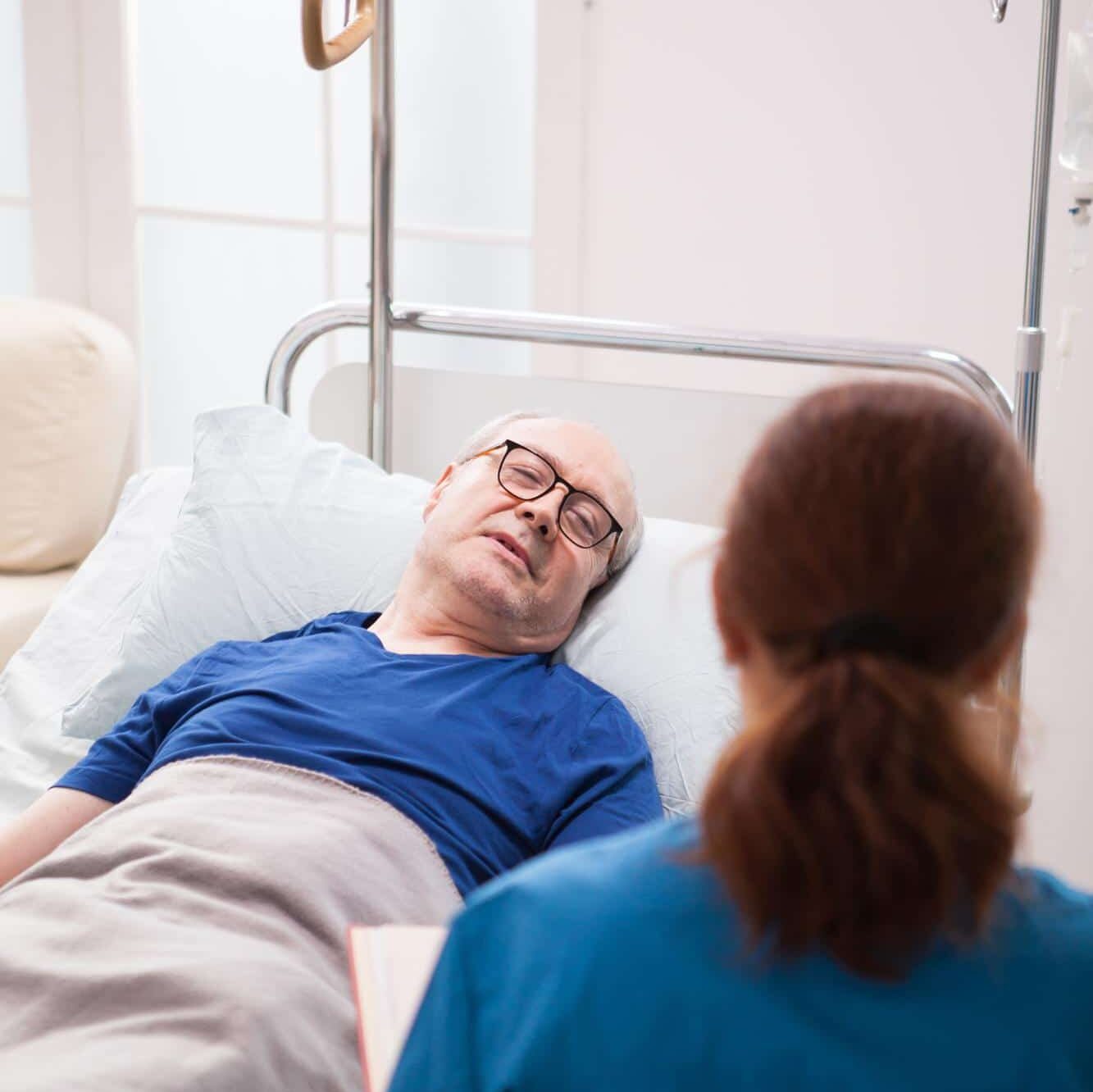 Älterer Mann im Krankenhausbett - Krankenschwester sitzt davor